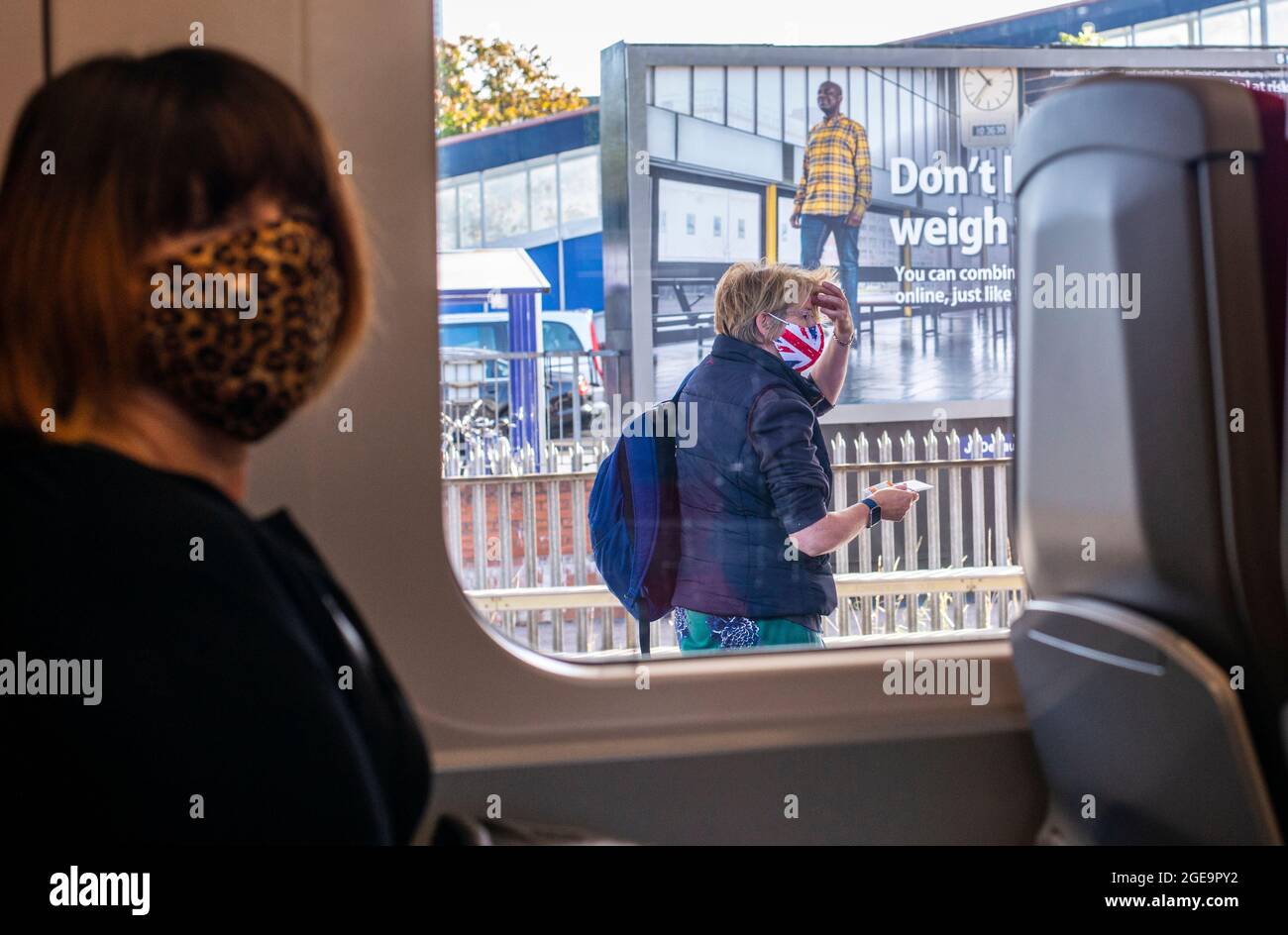 Eine Frau, die ein Gesicht von Union Jack trägt, fährt auf einem Bahnsteig vorbei, während eine andere Frau in einem Zug in Richtung Kamera schaut. Stockfoto