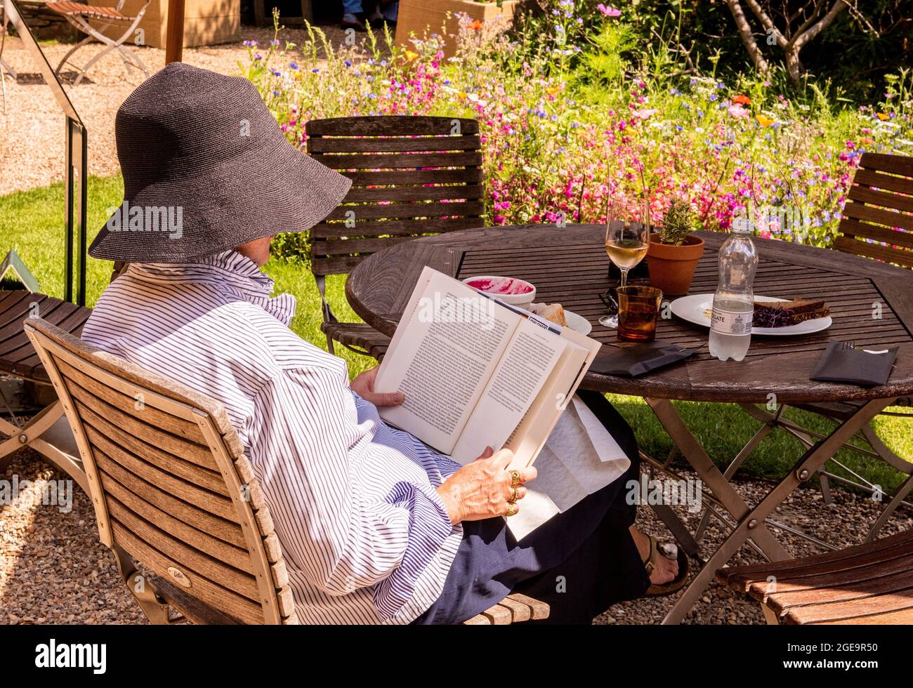 Eine Frau mit einem großen Sonnenhut liest friedlich im Café des Chelsea Physic Garden im Zentrum von London. Stockfoto