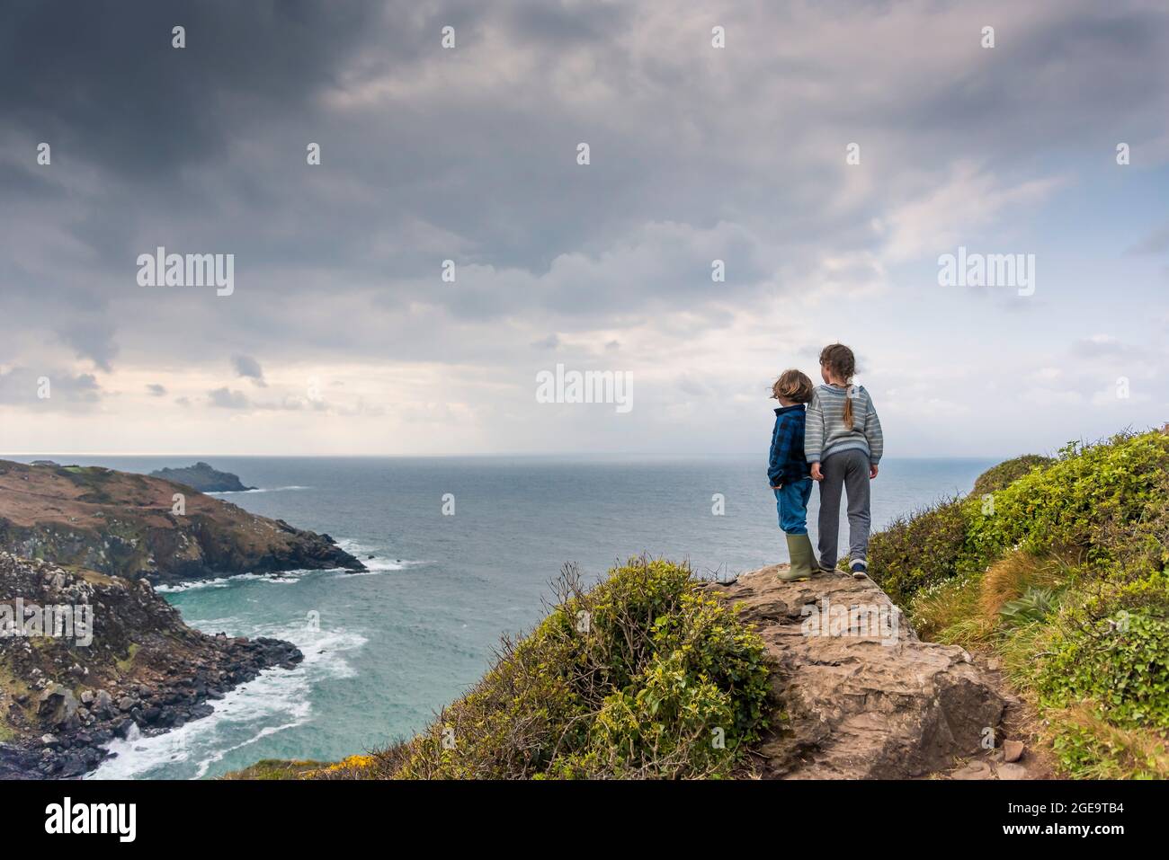 Zwei Kinder stehen auf Zennor Head und blicken über das Meer nach Gurnard's Head an der Küste von West Penwith in Cornwall. Stockfoto
