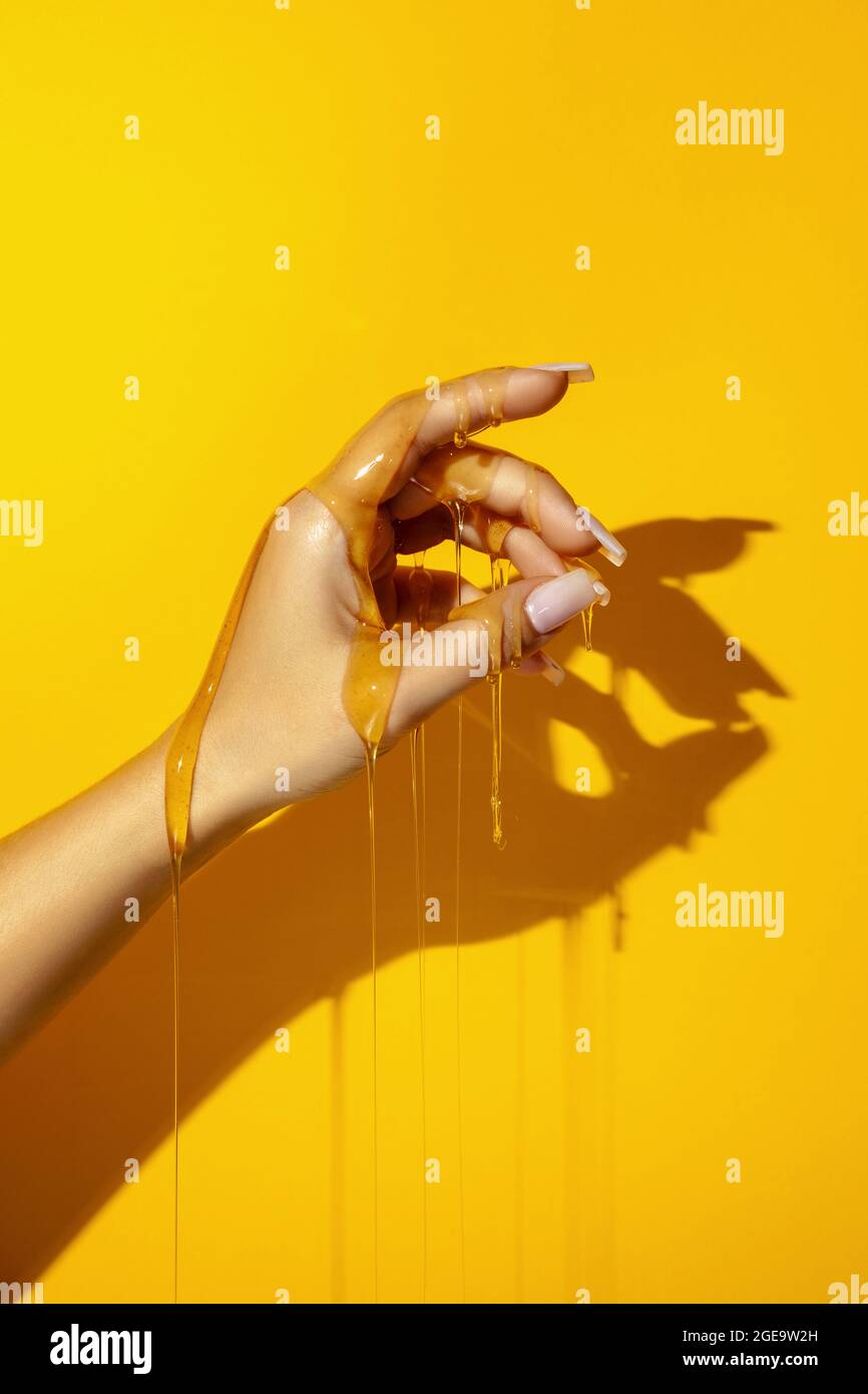 Crop unkenntlich weiblich zeigen Hand mit Maniküre und aromatischen Honigflüssigkeiten auf gelbem Hintergrund mit Schatten Stockfoto