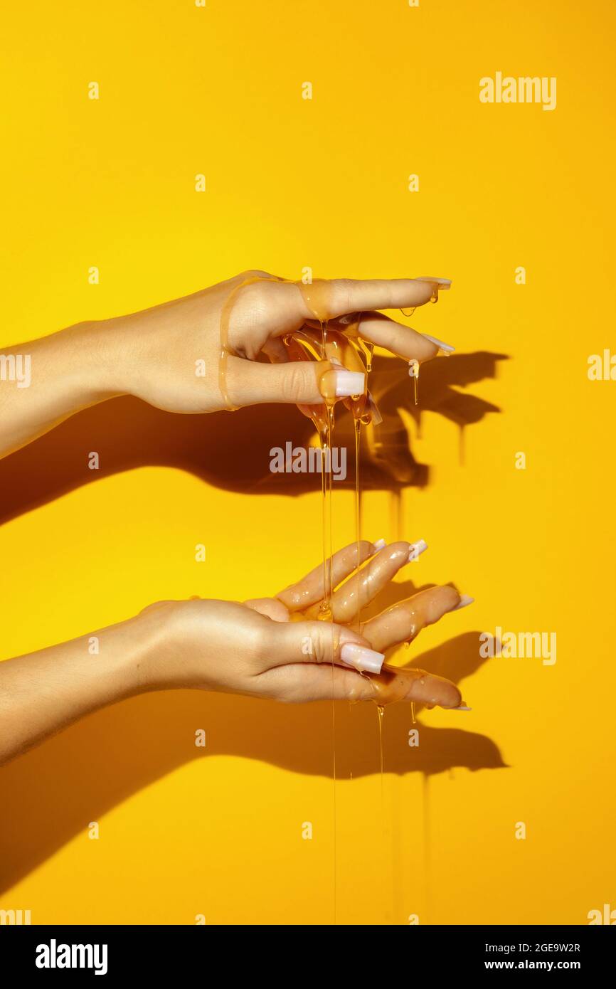 Crop unkenntlich weiblich zeigen Hand mit Maniküre und aromatischen Honigflüssigkeiten auf gelbem Hintergrund mit Schatten Stockfoto
