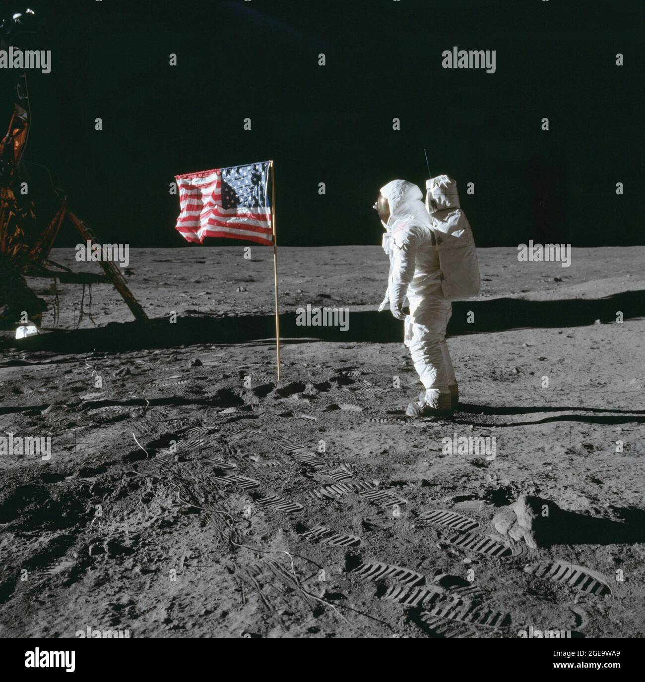 Astronaut Edwin E. Aldrin, Pilot der Mondlandefähre (LM), posiert für ein Foto neben der US-Flagge, die auf den Mond gesetzt wurde. Der LM ist im linken Sichtfeld sichtbar. Zahlreiche Fußabdrücke und das Kabel der Surface-Fernsehkamera sind auf der Mondoberfläche im Vordergrund zu sehen. Aufnahme auf der Tranquility Base während der Apollo 11 Mission. Das Original-Filmmagazin wurde mit der Bezeichnung S. Filmtyp: Ektachrome EF SO168 Farbfilm auf einer 2.7-mil-Estarbasis aus Polyester, aufgenommen mit einem 60-mm-Objektiv. Der Sonnenwinkel ist „Mittel“. Neigungsrichtung ist Süden (S). Stockfoto