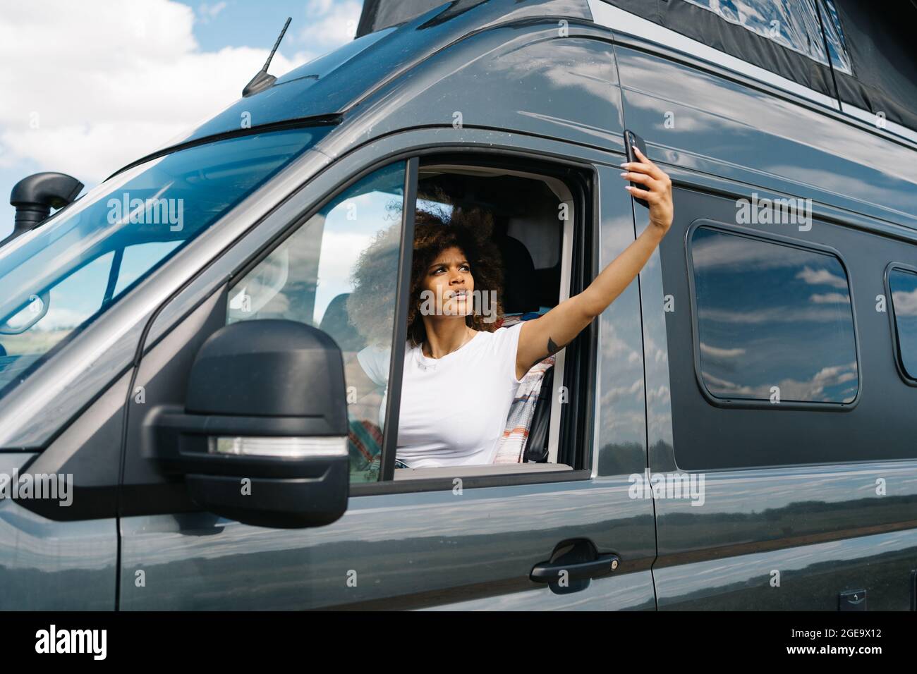 Unglückliche junge afroamerikanische Reisende, die auf dem Fahrersitz im Wohnmobil sitzt und versucht, eine Verbindung über das Mobiltelefon zu bekommen, während sie Probleme hat Stockfoto