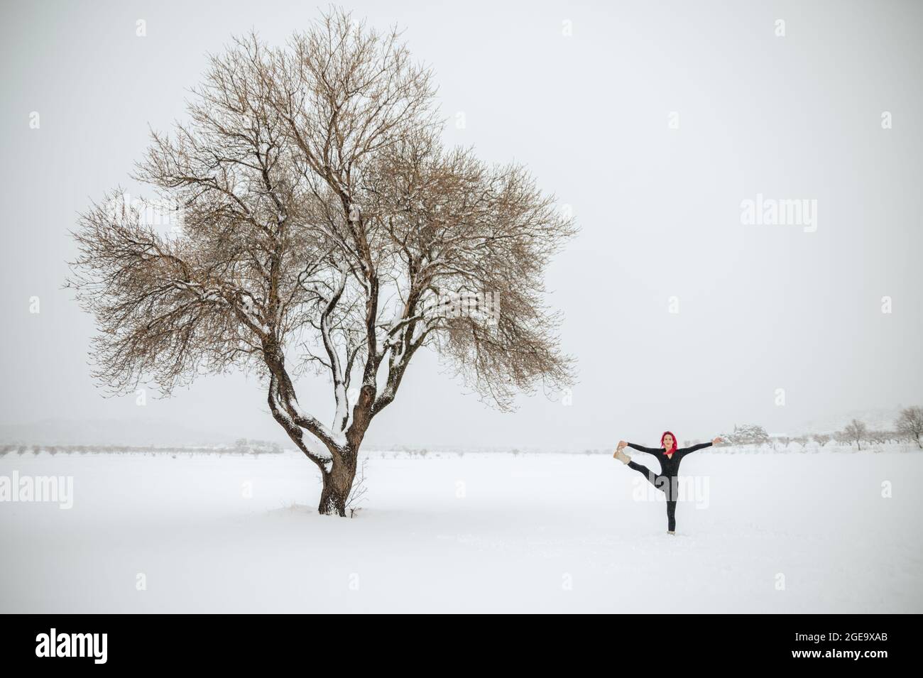 Fernansicht einer flexiblen Frau, die in Utthita Hasta Padanguschthasana Yoga praktiziert, während sie im Winter auf einem verschneiten Feld steht Stockfoto