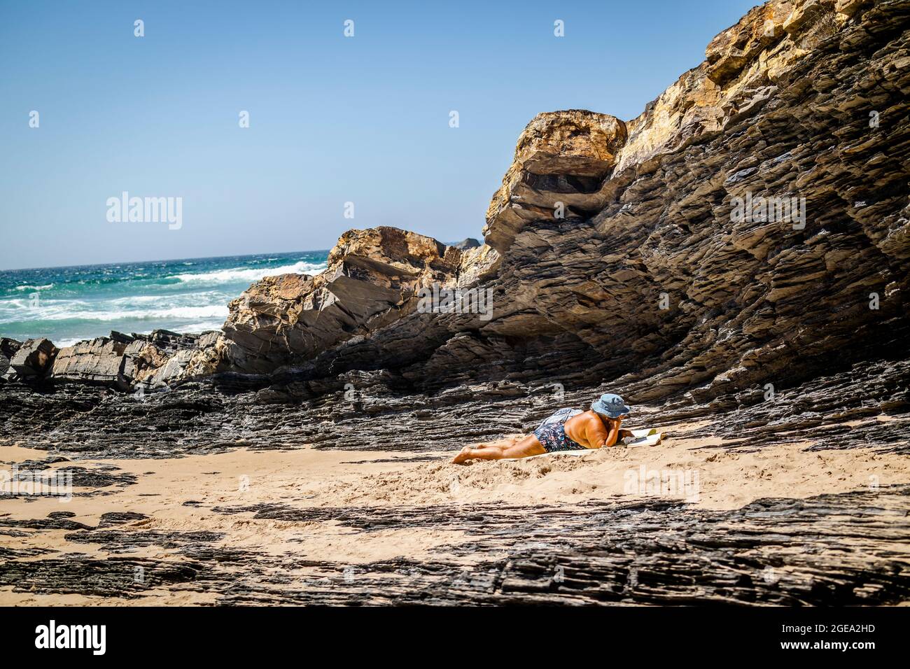 Ältere Frau, die sich in Zambujeira do Mar, Naturpark Vicentina-Küste, Alentejo, Portugal, an den Felsen entspannt Stockfoto