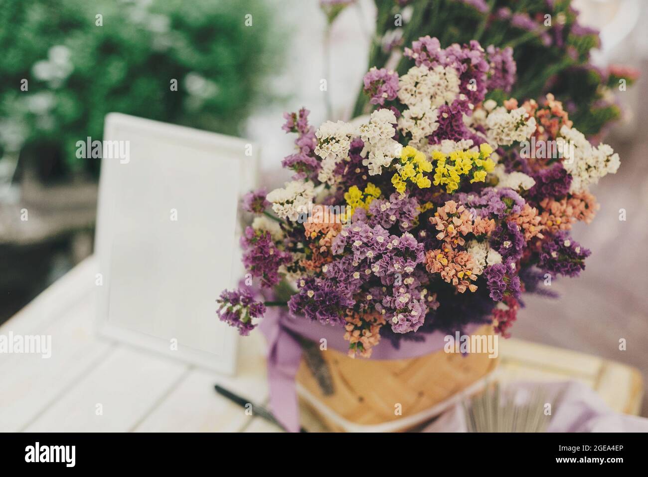 Stilvoller rustikaler Hochzeitsstrauß und weißer Rahmen auf dem Tisch beim Hochzeitsempfang im Restaurant. Bunte Blumen und Gästebuch für Wünsche. Einrichtung und Service Stockfoto