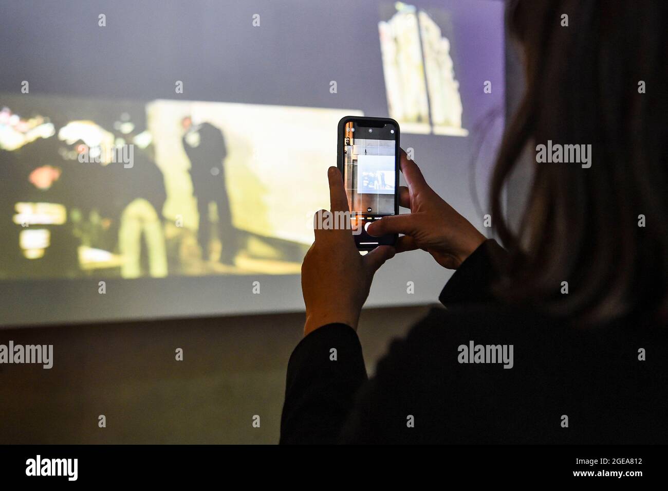 18. August 2021, Berlin: Eine Besucherin fotografiert mit ihrem Handy die Installation eines Videos von Eduard Freudmann mit dem Titel 'Shame Watch'. Auf dem Gelände des Holzmarktes in Berlin eröffnet die multimediale Kunstausstellung „Transitions“, die Werke von 18 jüdischen Künstlern aus Europa und Amerika präsentiert. Es beginnt mit dem Festival zeitgenössischer jüdischer Kunst, das Lesungen, Performances, die Ausstellung, Diskussionen, Und Workshops. Foto: Kira Hofmann/dpa-Zentralbild/dpa - ACHTUNG: Nur für redaktionelle Verwendung im Zusammenhang mit einem Ausstellungsbericht und nur mit vollständiger Erwähnung des Abov Stockfoto