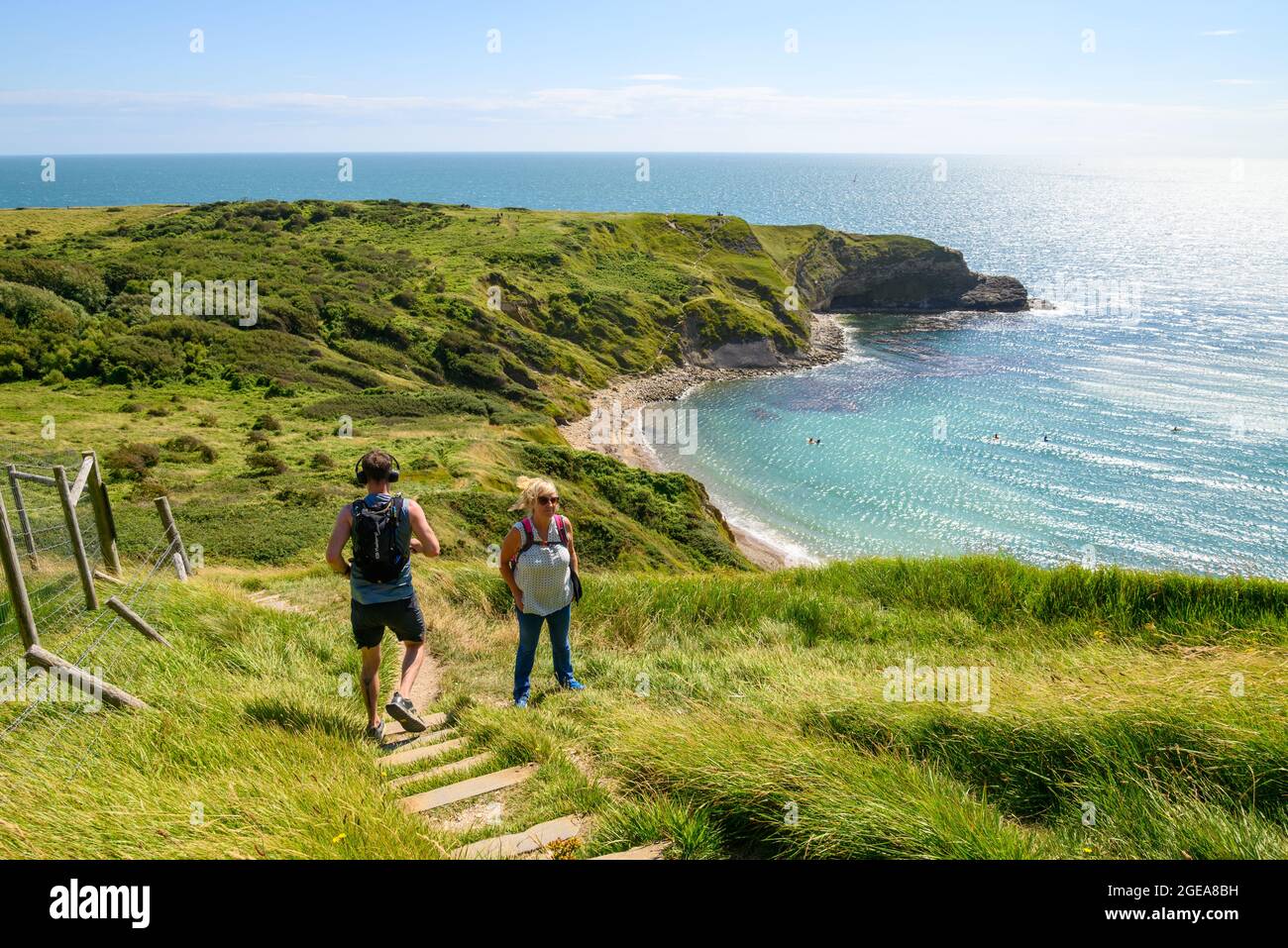 Mann, der einen steilen Hügel hinunterläuft, vorbei an einer Frau, die auf einem steilen Abschnitt des South West Coast Path in Lulworth Cove, West Lulworth, Dorset, Großbritannien, bergauf geht Stockfoto