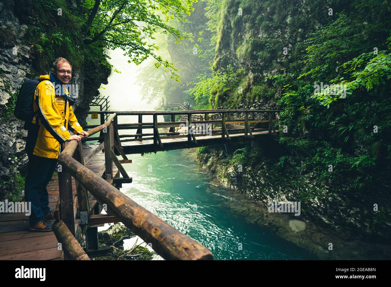 Wanderweg entlang des klaren Flusses durch die Vintgar-Schlucht in Slowenien mit Mann im gelben Mantel Stockfoto