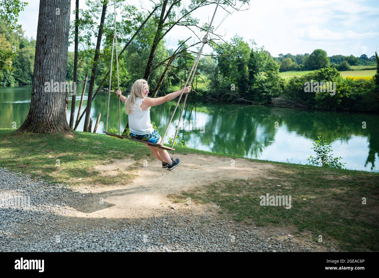 Blonde Frau auf einer riesigen Schaukel mit Blick auf einen grünen Fluss während der Sommerferien - ein glücklicher Tag frei Stockfoto