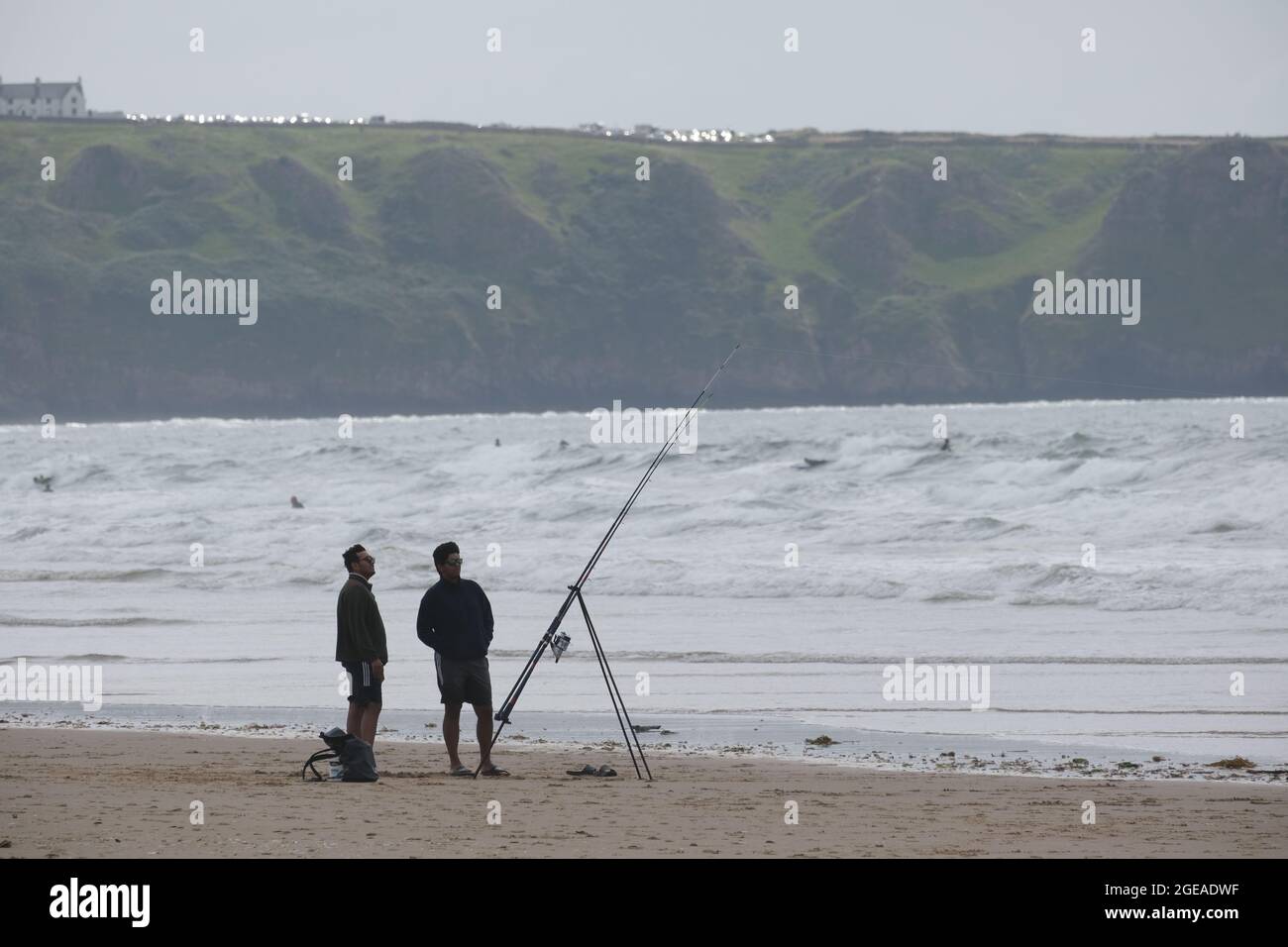 Gower, Swansea, Großbritannien. August 2021. Strandbesucher genießen am Strand Llangennith auf der Halbinsel Gower das Beste aus den für die Saison unbeständig kühlen Temperaturen und den windigen Bedingungen. Zwei Fischer beobachten ihre Ruten im Falle eines Bisses. Kredit: Gareth Llewelyn/Alamy Stockfoto