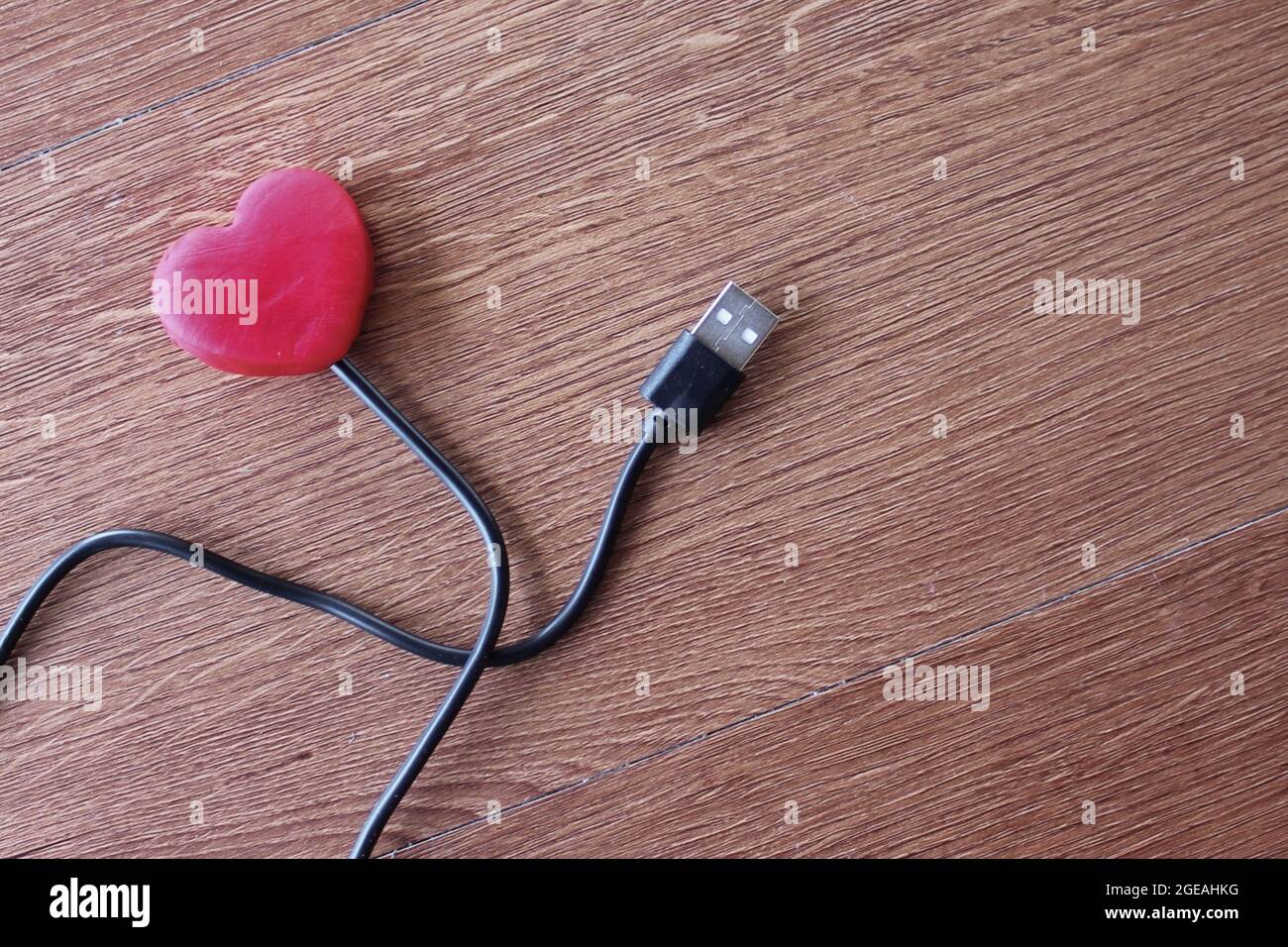 Rotes Herz mit usb-Kabel auf Holzhintergrund. Liebe und Technologie Konzept Stockfoto