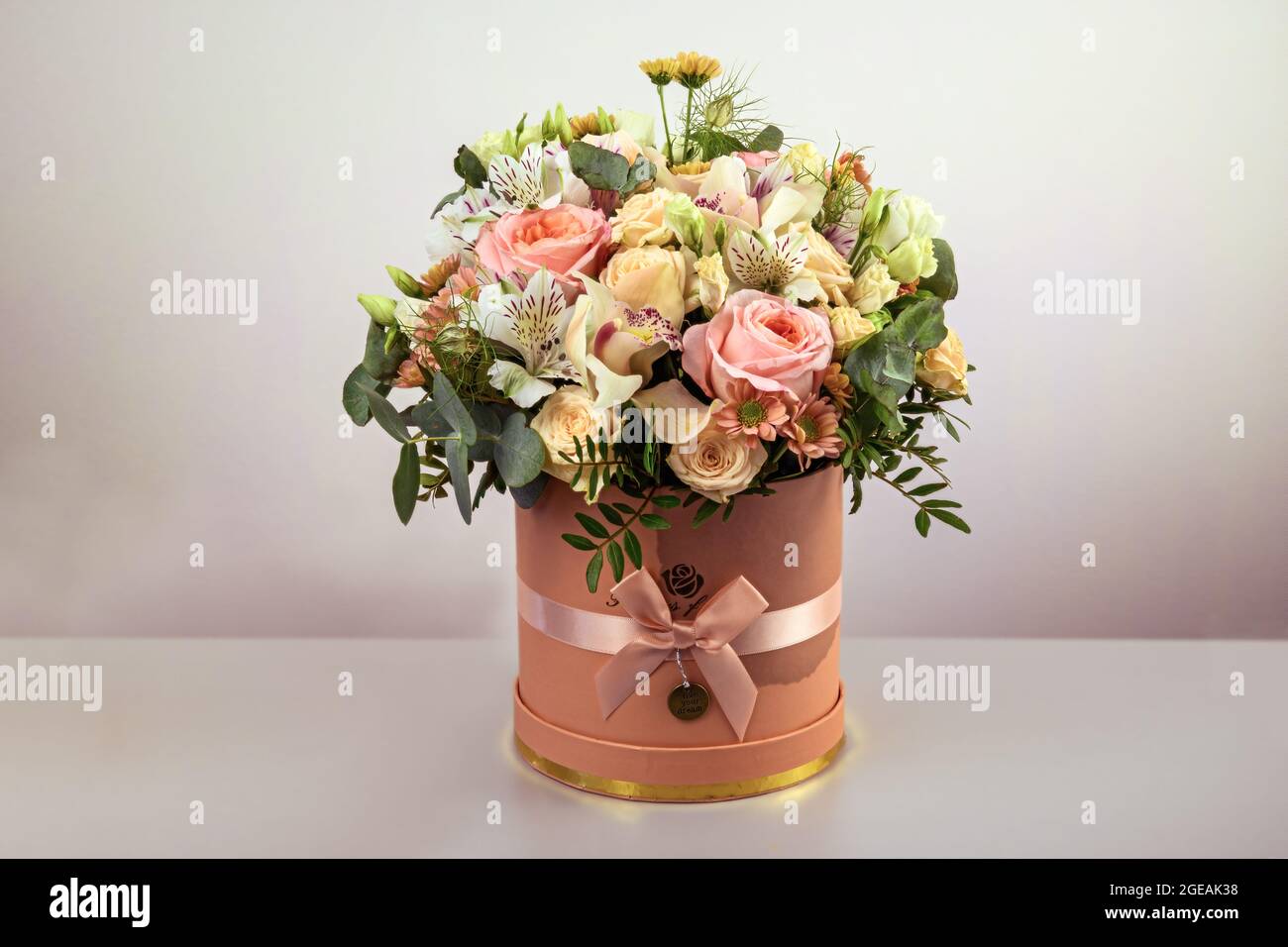 Ein schöner Strauß zarter Blüten aus rosa Rosen, weißen Lilien und gelben Gerberas in einer handgefertigten Schachtel. Alles ist mit grünen palmenlea dekoriert Stockfoto