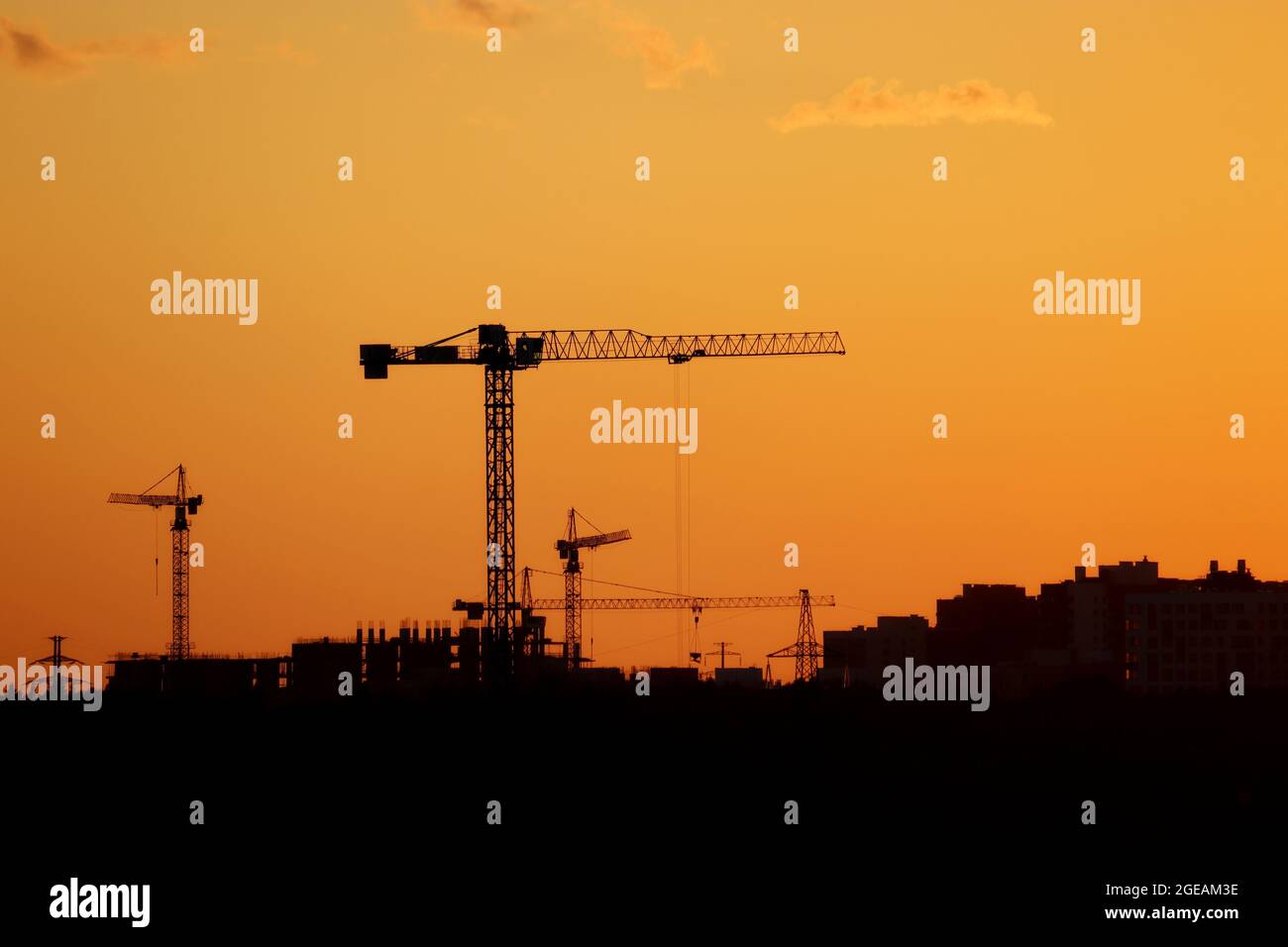 Silhouetten von Baukräne und Wohngebäuden auf orangefarbenem Sonnenuntergang am Himmel. Wohnungsbau, Wohnblock in der Stadt Stockfoto