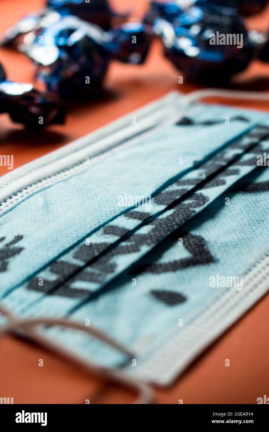 Halloween-Wort auf einer medizinischen Maske und einige Pralinen in ihren Verpackungen auf einer orangefarbenen Oberfläche geschrieben Stockfoto