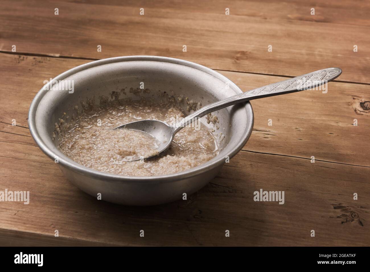 Schlechtes Essen. Getreidebrei auf Wasser in der alten Aluminiumschüssel auf dem Holztisch Stockfoto