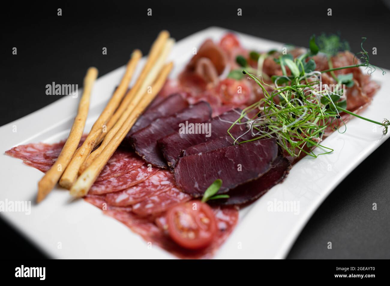 Kalte Fleischplatte mit Salami, Prosciutto und Brotstäbchen auf schwarzem Hintergrund Stockfoto