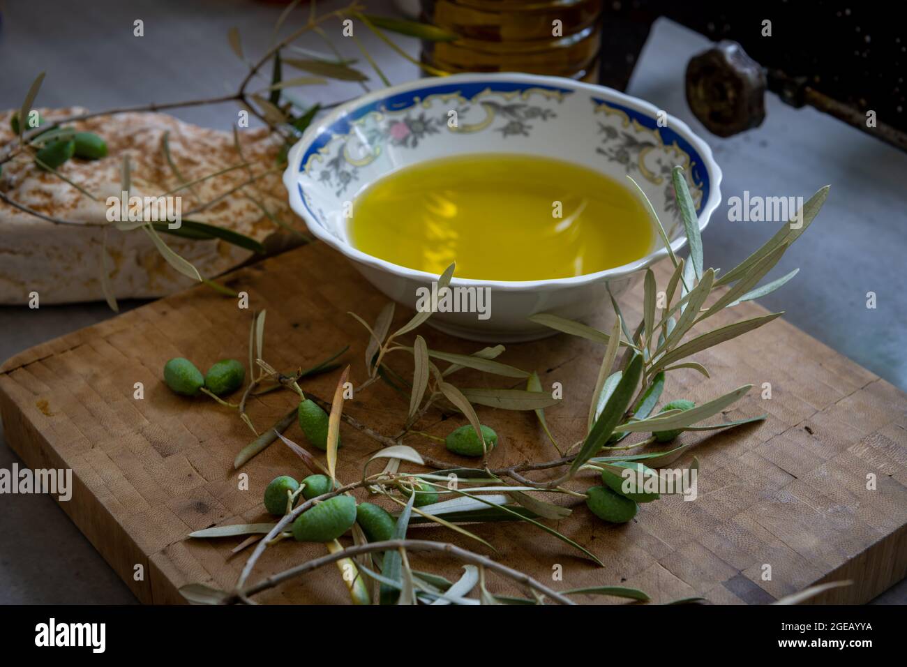 Grüne Oliven und Zweig auf einem Holzbrett mit einer Schüssel und einer Flasche heimisch kalt gepresstes Olivenöl. Stockfoto
