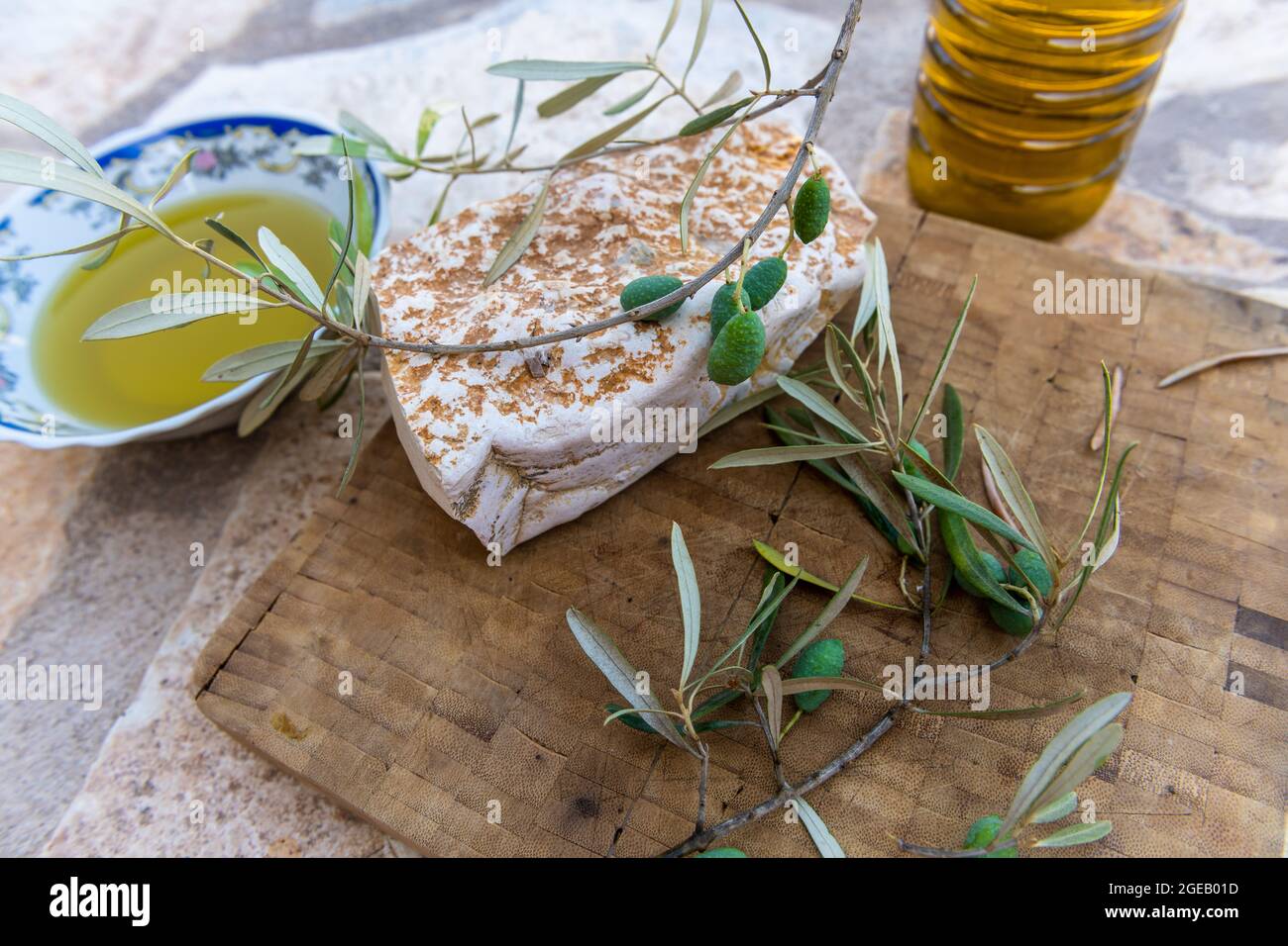 Grüne Oliven und Zweig auf einem Holzbrett mit einer Schüssel und einer Flasche heimisch kalt gepresstes Olivenöl. Stockfoto