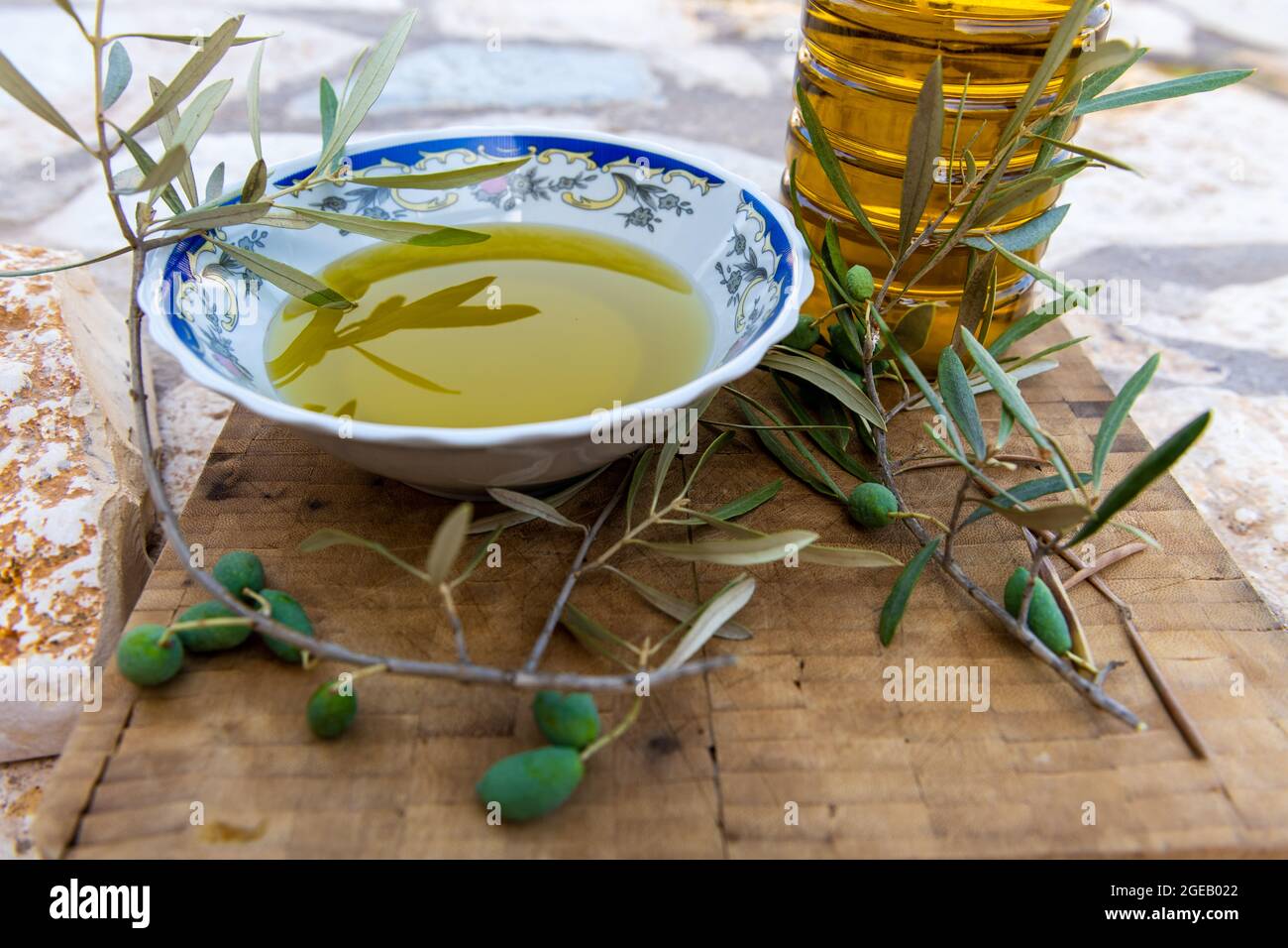 Grüne Oliven und Zweig auf einem Holzbrett mit einer Schüssel und einer Flasche heimisch kalt gepresstes Olivenöl. Stockfoto