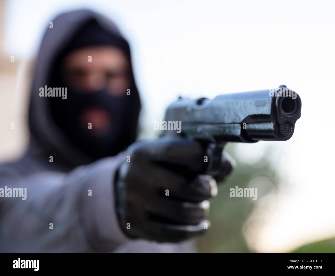 Killer mit Sturmhaube, hält eine Waffe in der Hand mit Handschuhen, bewaffnete Räuber Konzept. Mann, der mit einer Pistole anvisierte, Natur im Hintergrund, Nahaufnahme. Stockfoto