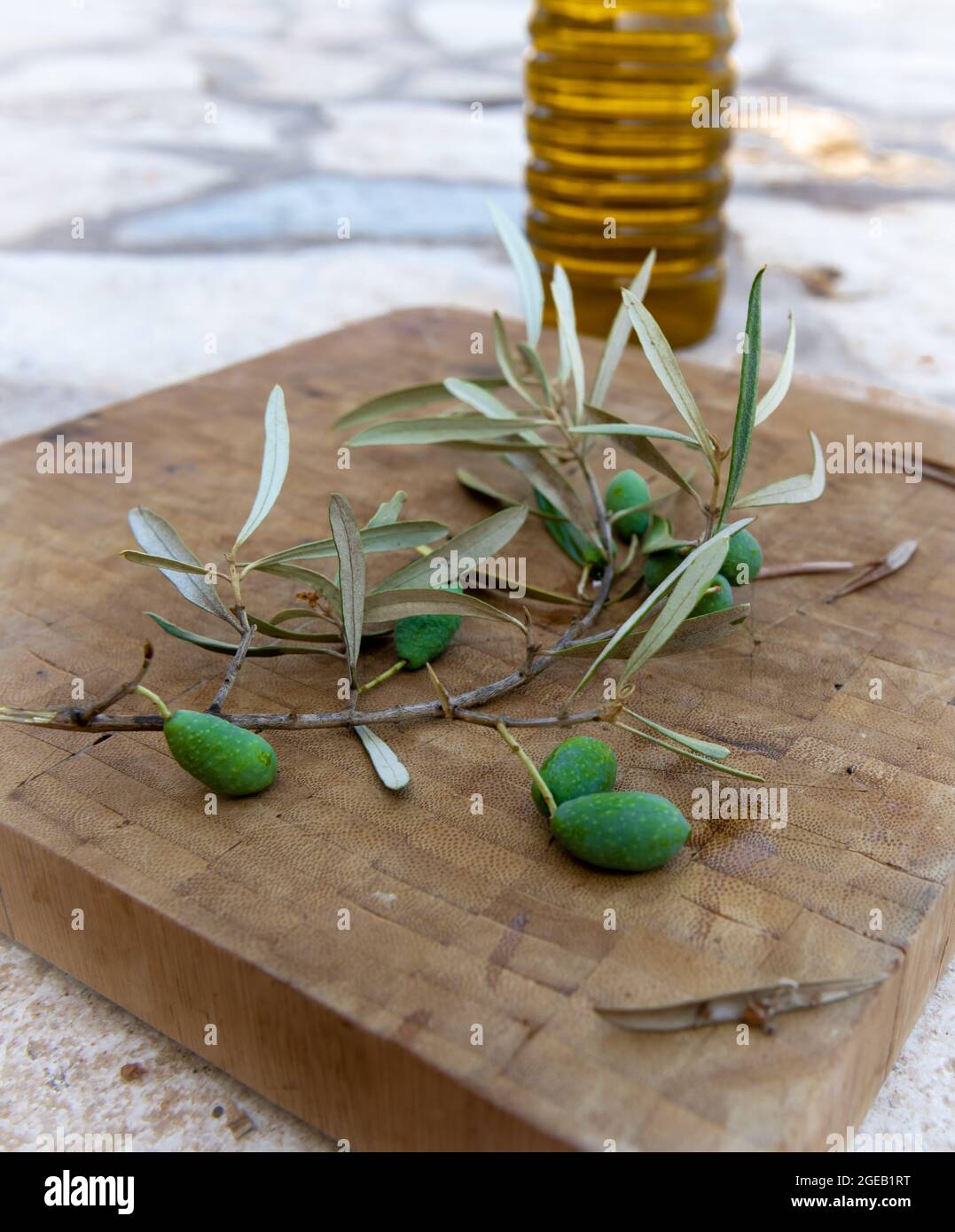 Grüne Oliven und Olivenzweig auf einem Holzbrett mit einer Flasche Olivenöl. Stockfoto