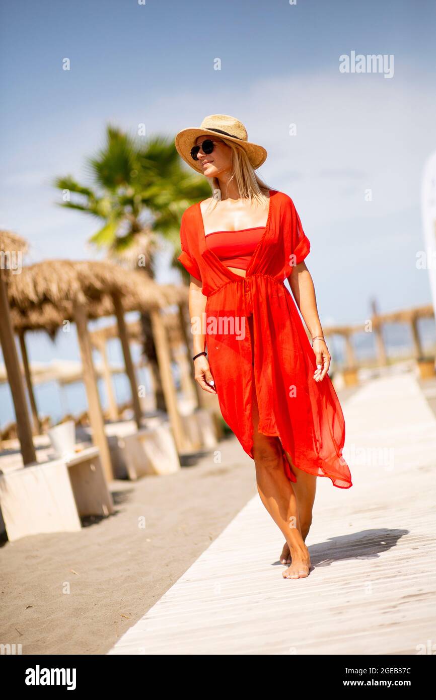 Hübsche junge Frau in rotem Kleid, die im Sommer am Strand spazieren geht Stockfoto