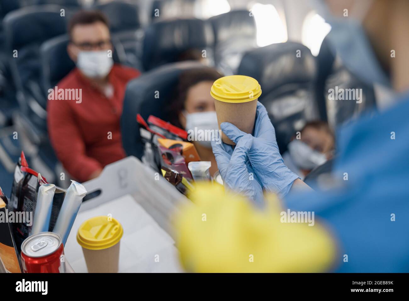 Nahaufnahme der Hände in Schutzhandschuhen des Flugbegleiters, der den Passagieren an Bord Getränke serviert. Reisen mit dem Flugzeug während der Covid19-Pandemie Stockfoto
