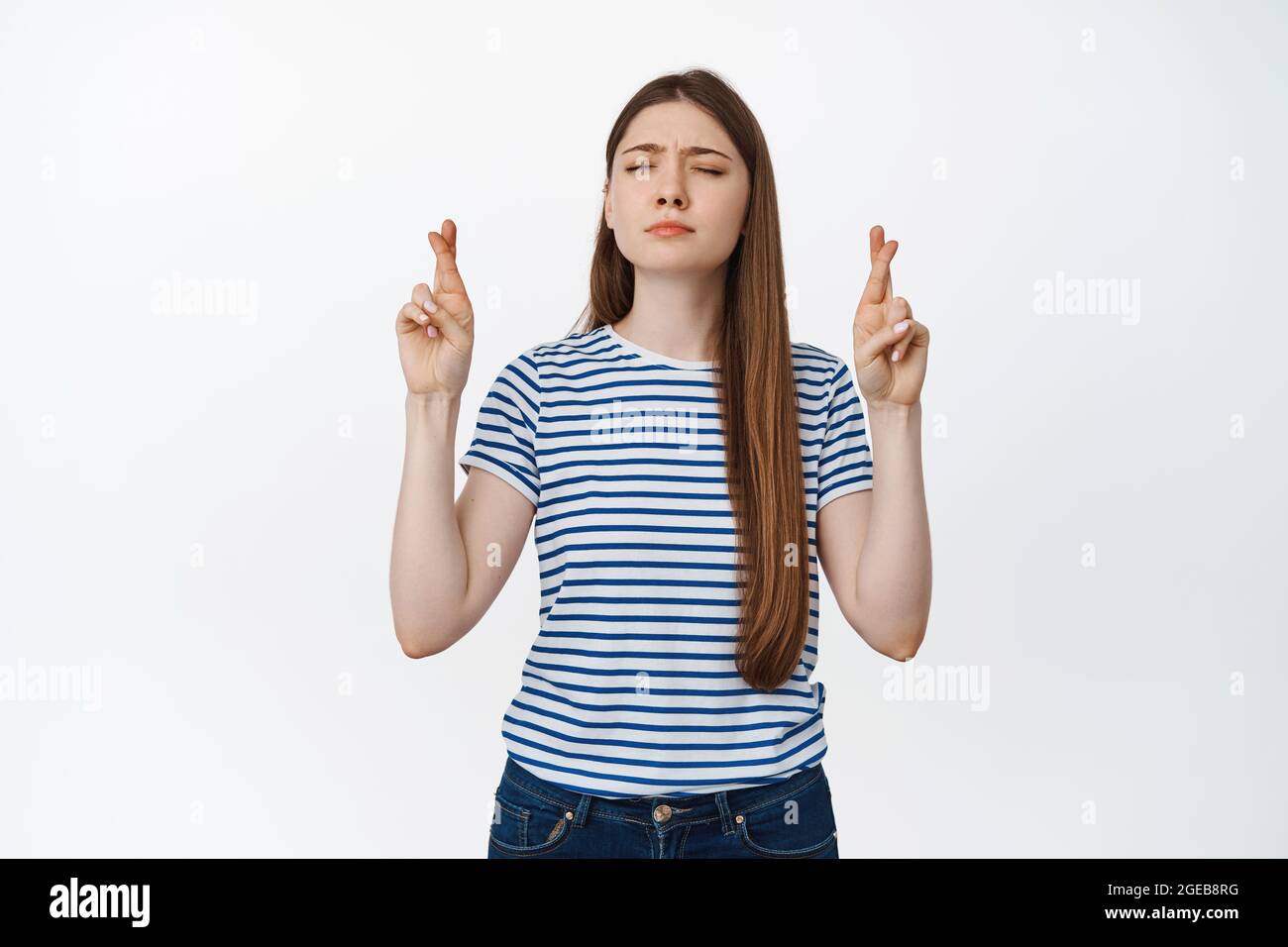 Hoffnungsvolle junge Frau kreuzt die Finger und bettelt, Wünsche machend, Nachrichten vorwegnehmend, weißer Hintergrund Stockfoto