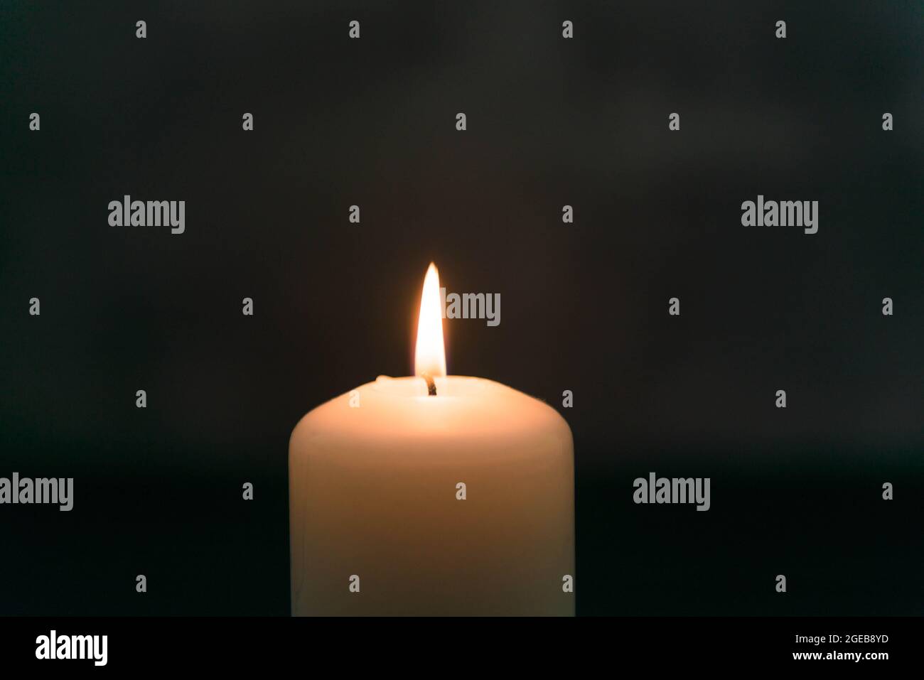 Weiße Kerze im Dunkeln auf dunklem Hintergrund. Die Kerzenflamme strahlt warmes gelbes Licht aus. Stockfoto