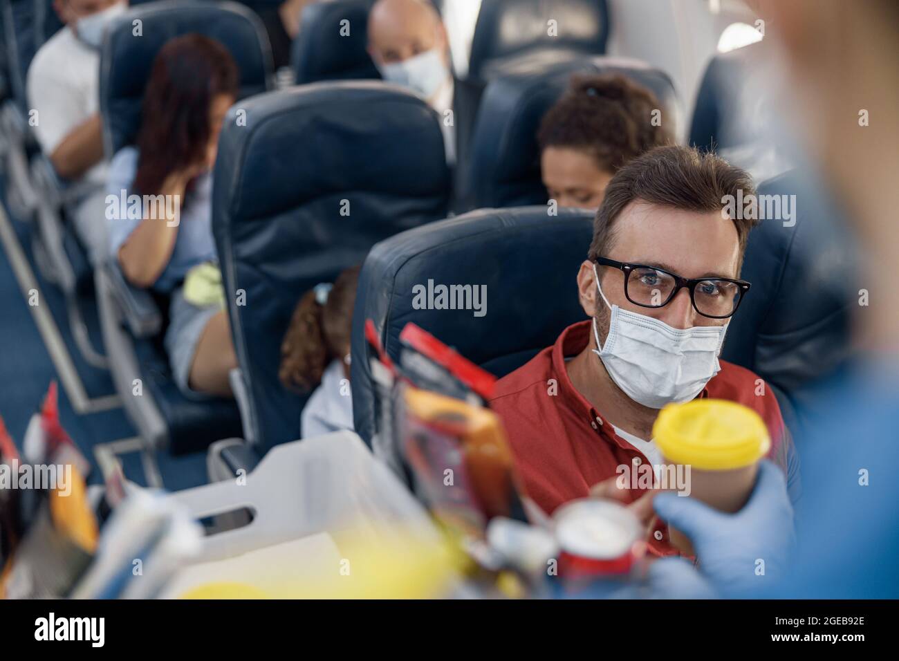 Flugbegleiter serviert dem männlichen Passagier Getränke in einer schützenden Gesichtsmaske an Bord. Reisen mit dem Flugzeug während der Covid19-Pandemie Stockfoto