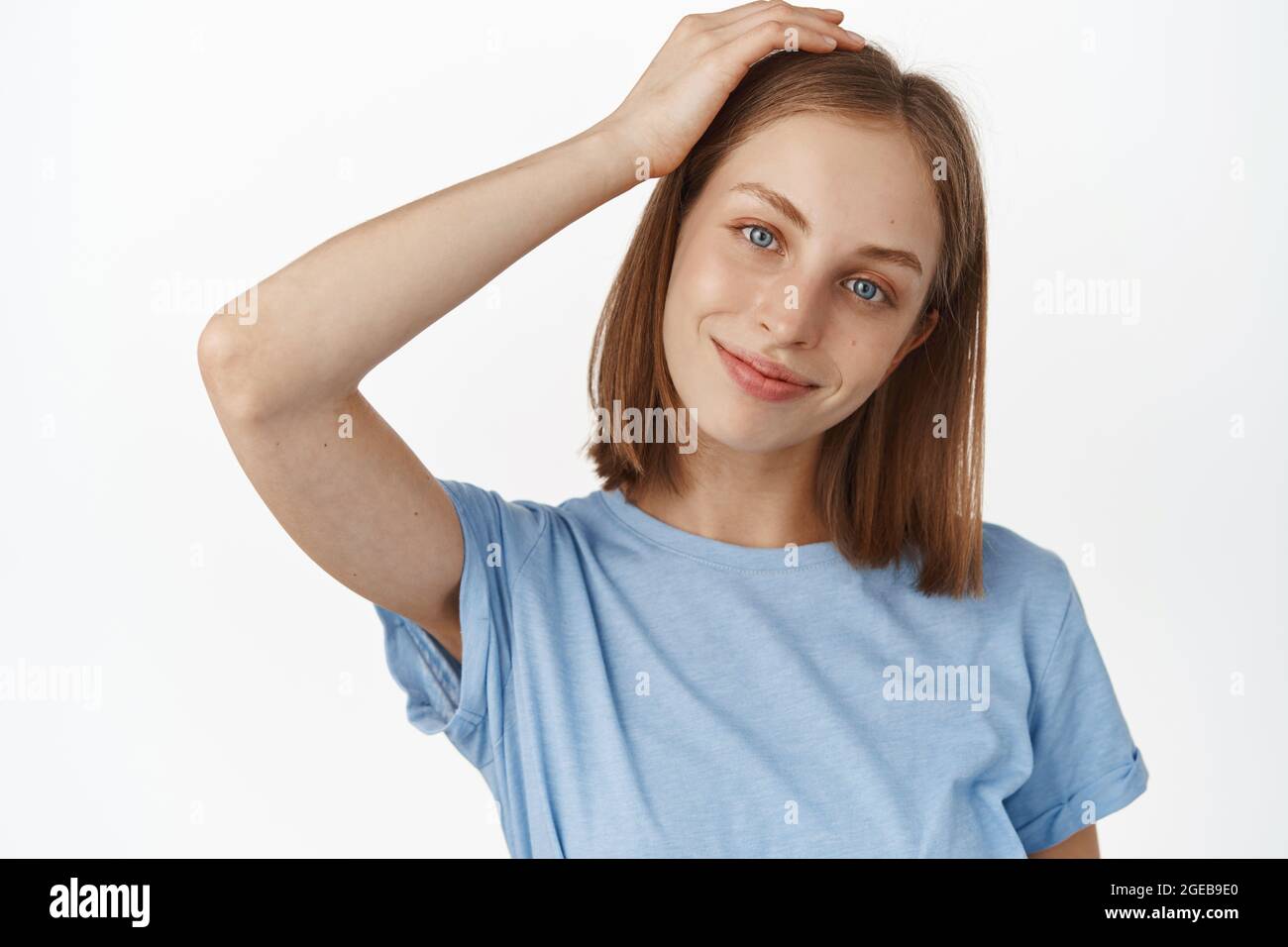 Hautpflege Routine und Schönheit. Fröhliches junges blondes Mädchen berührt ihre Frisur, lächelt und schaut auf die Kamera zart, hübsches Gesicht mit natürlichem Glanz und nein Stockfoto