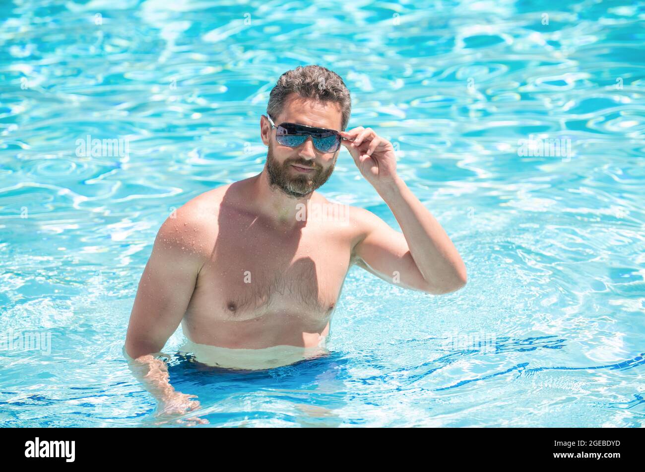 Glücklicher bärtiger Mann in einer Brille, der im Sommer im Pool schwimmt, entspannen Sie sich Stockfoto
