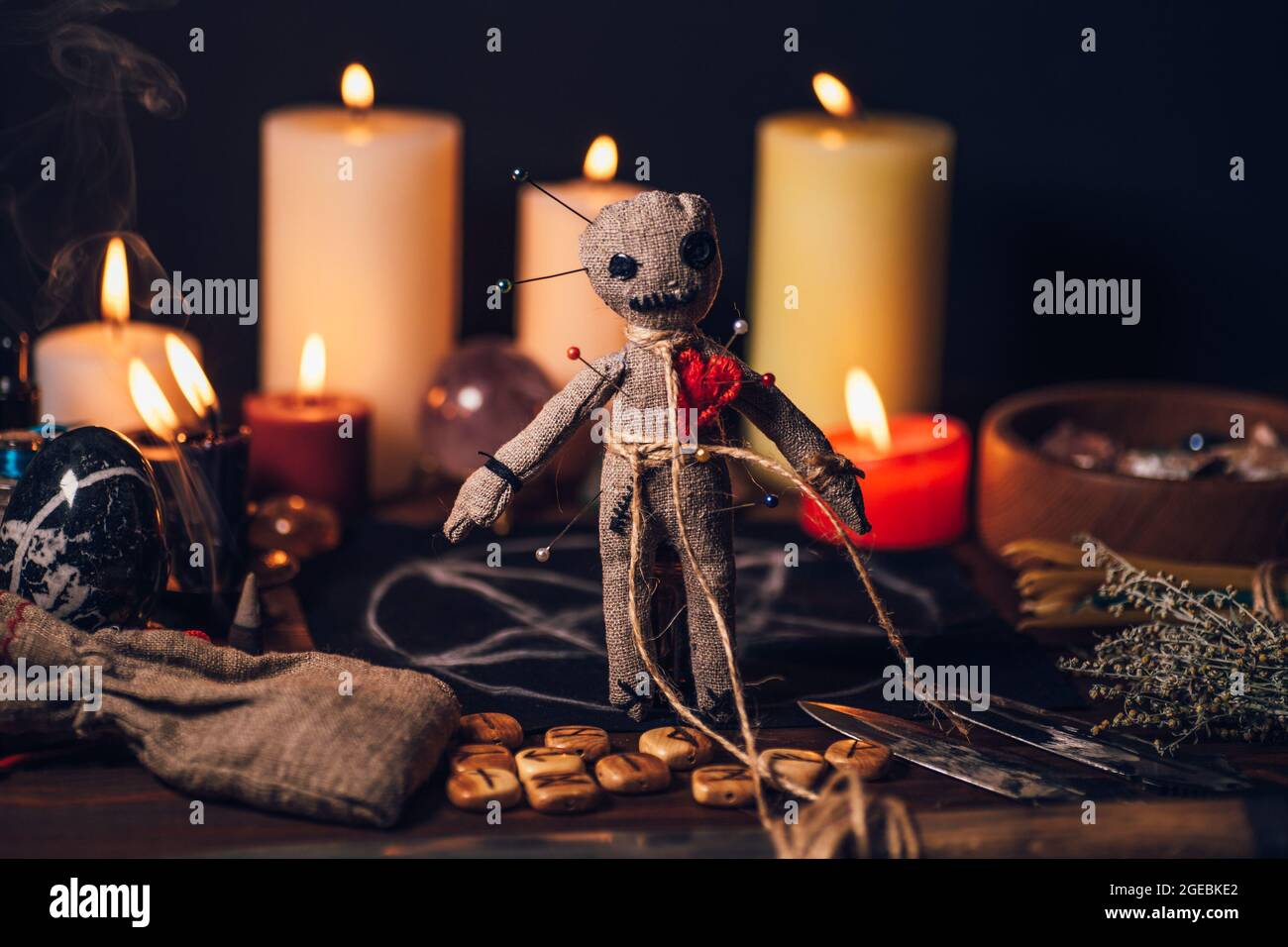 Voodoo-Puppe auf einem magischen Tisch mit esoterischen Objekten und brennenden Kerzen für ein magisches Racheritual. Stockfoto