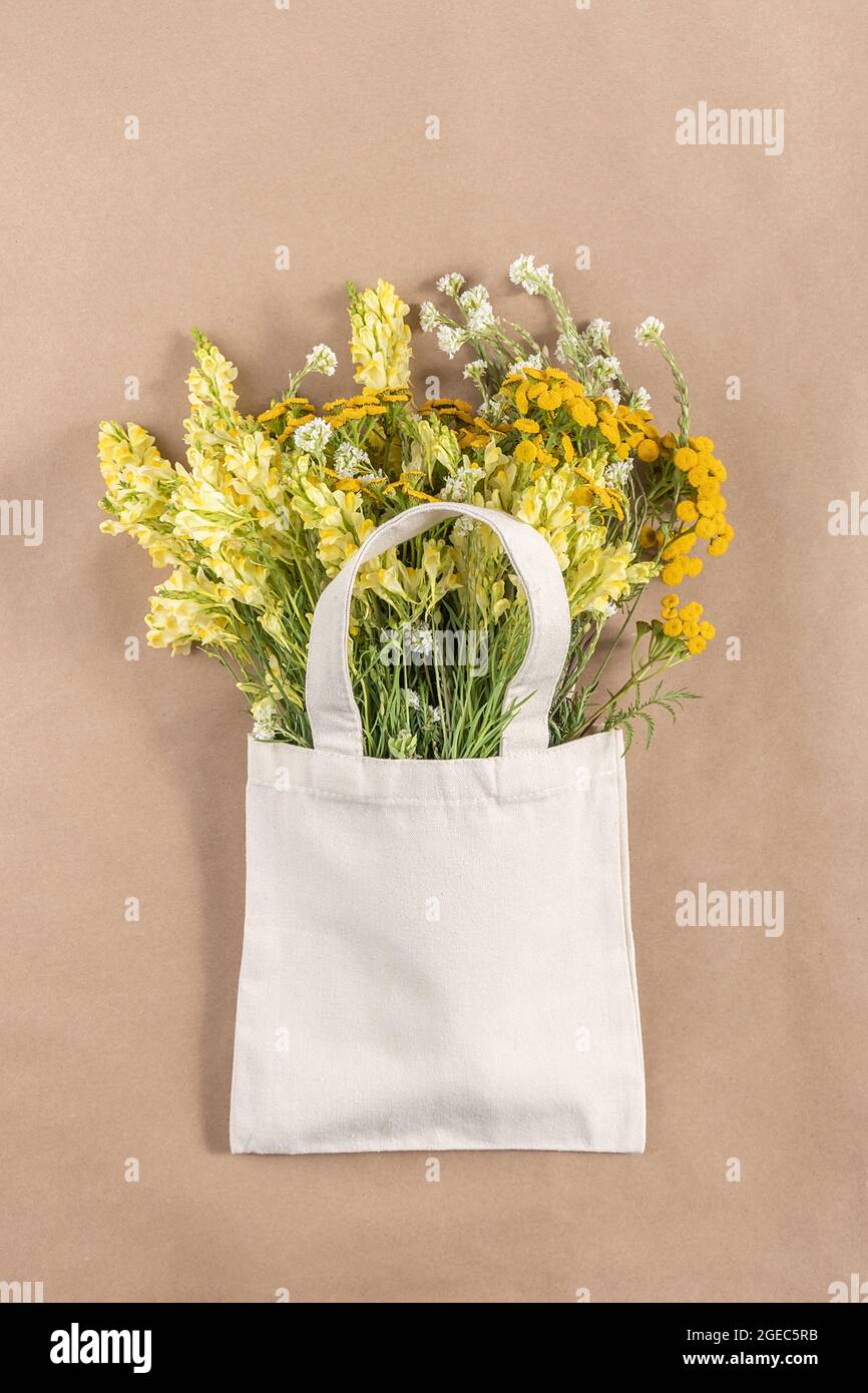 Bouquet von Feldblumen in Stoff Öko-Tasche auf beigem Hintergrund. Konzept kein Kunststoff und kein Abfall. Mockup von oben. Stockfoto