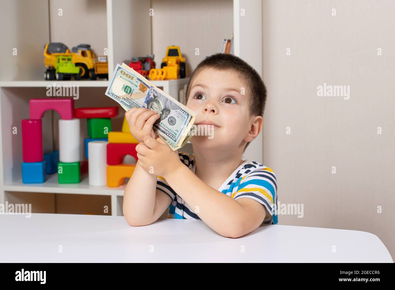 Ein schönes Kind und Dollarscheine. Der Junge denkt darüber nach, wo er das Geld ausgeben soll. Finanzielle Bildung für Kinder Stockfoto