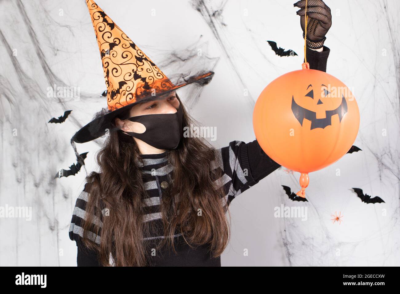 Halloween maskierte Menschen. Eine Frau in einem Hexenkostüm in einer  Schutzmaske hält einen Kürbisball. Während der Coronavirus-Pandemie  Stockfotografie - Alamy