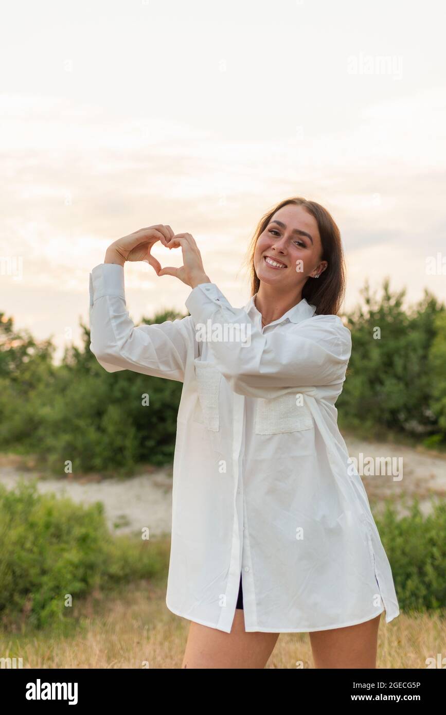 Junge Frau, die bei Sonnenuntergang eine Hand in Herzform auf einem Garten macht. Frau in der Natur hält Herz-Form-Symbol mit Hands.Love und Natur Beauty-Konzept gemacht Stockfoto