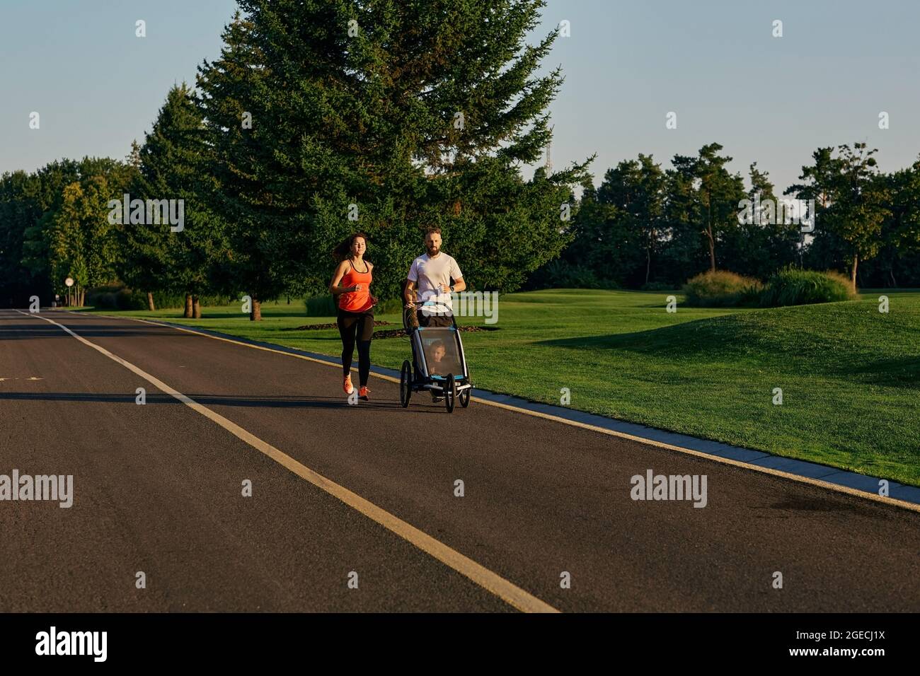 Aktives Familienleben. Junge Familie mit ihrem Kind in einem Jogging-Kinderwagen beim Joggen in einem öffentlichen Park Stockfoto