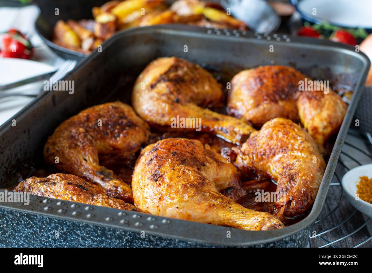 Gebratene Hähnchenschenkel mit einer köstlichen Tomatensoße, die in einer Backform auf dem Küchentisch serviert wird Stockfoto