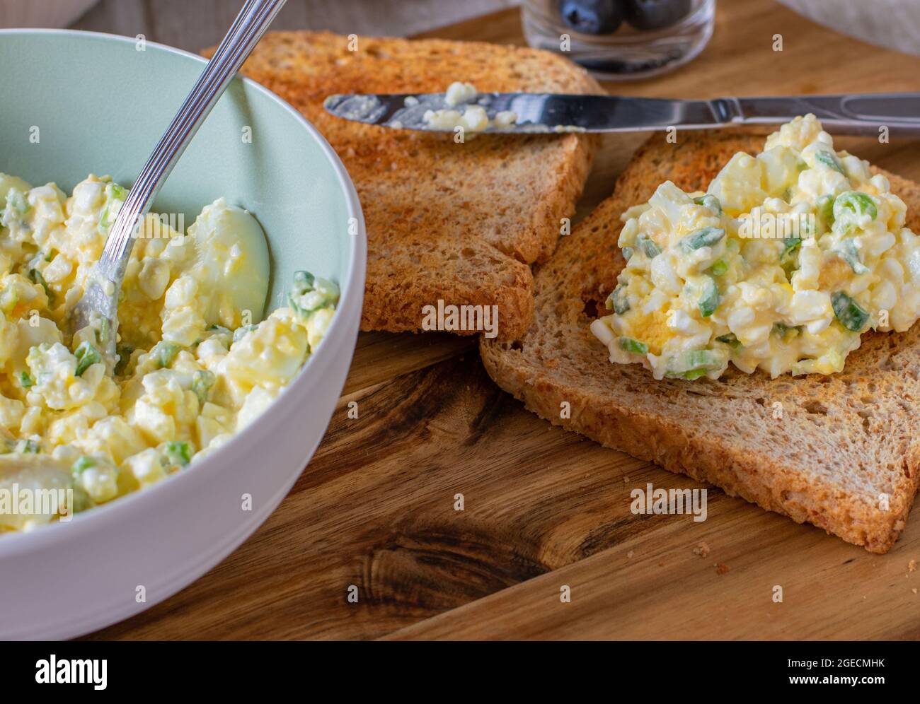 Fettarmer Eiersalat mit Quark, gekochten und gehackten Eiern und Schnittlauch, serviert mit Vollkorn-Toast auf einem Holzbrett. Proteinreiches Gericht Stockfoto
