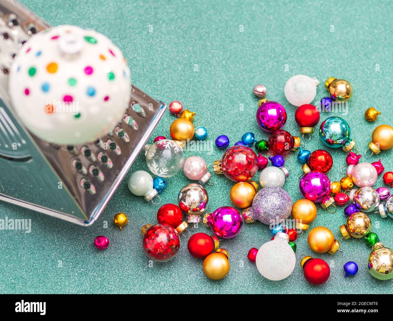 Konzeptionelles Foto, Weihnachtskugel auf Reibe für Gemüse mahlen auf grünem Glitzer glänzenden Hintergrund. Kochen oder bereiten Sie Weihnachten vor. Horizontales Foto wi Stockfoto