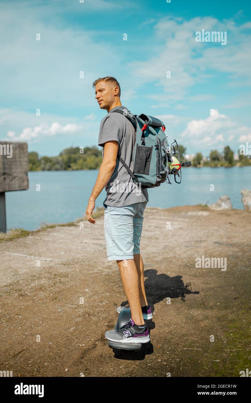 Mann mit Rucksack auf einem motorisierten Skateboard mit einem Rad auf dem Bürgersteig Stockfoto