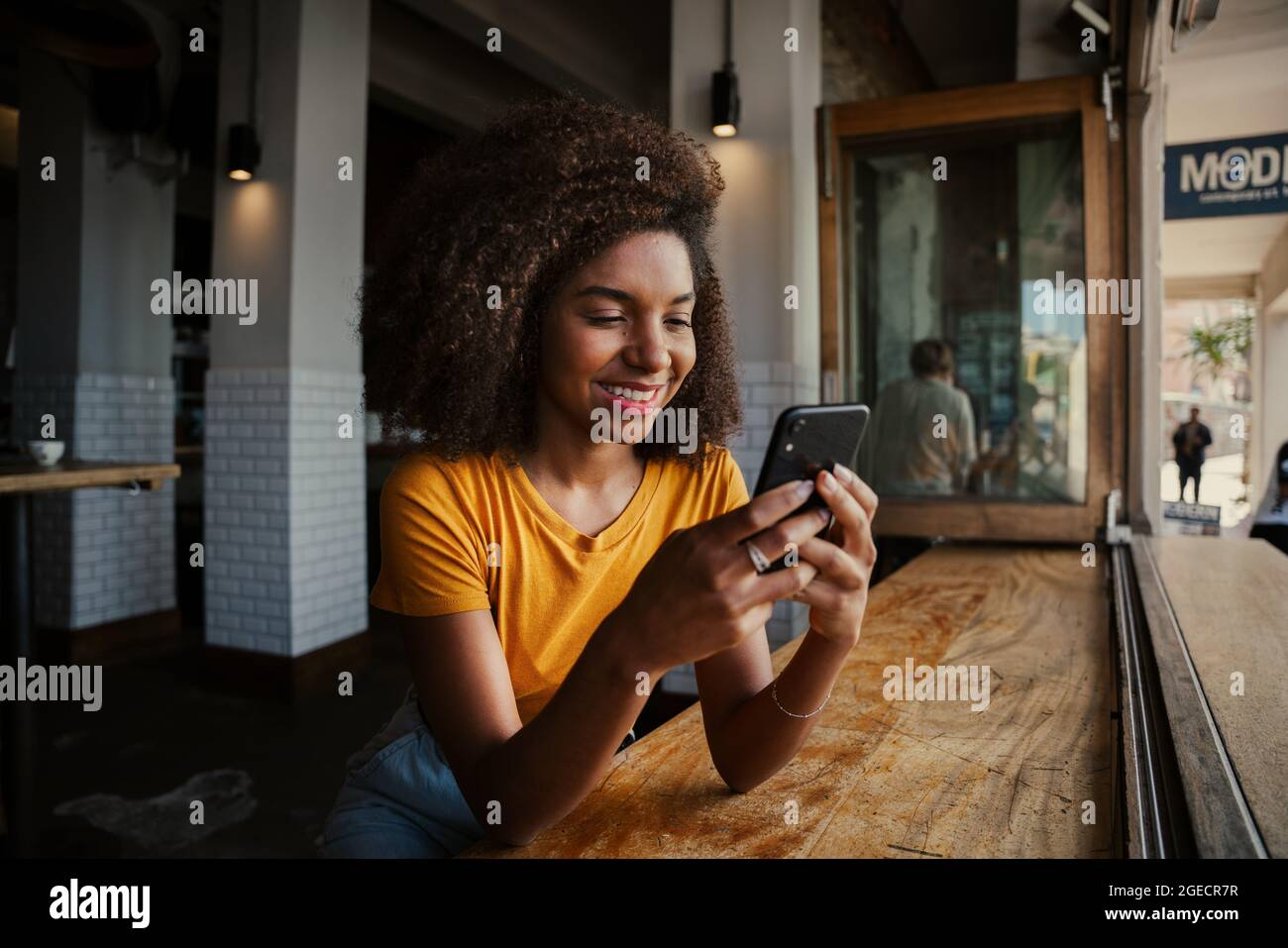 Lächelnde Kundin schreibt Smartphone-SMS-Mitschülern vom Smartphone, das im trendigen Café sitzt Stockfoto