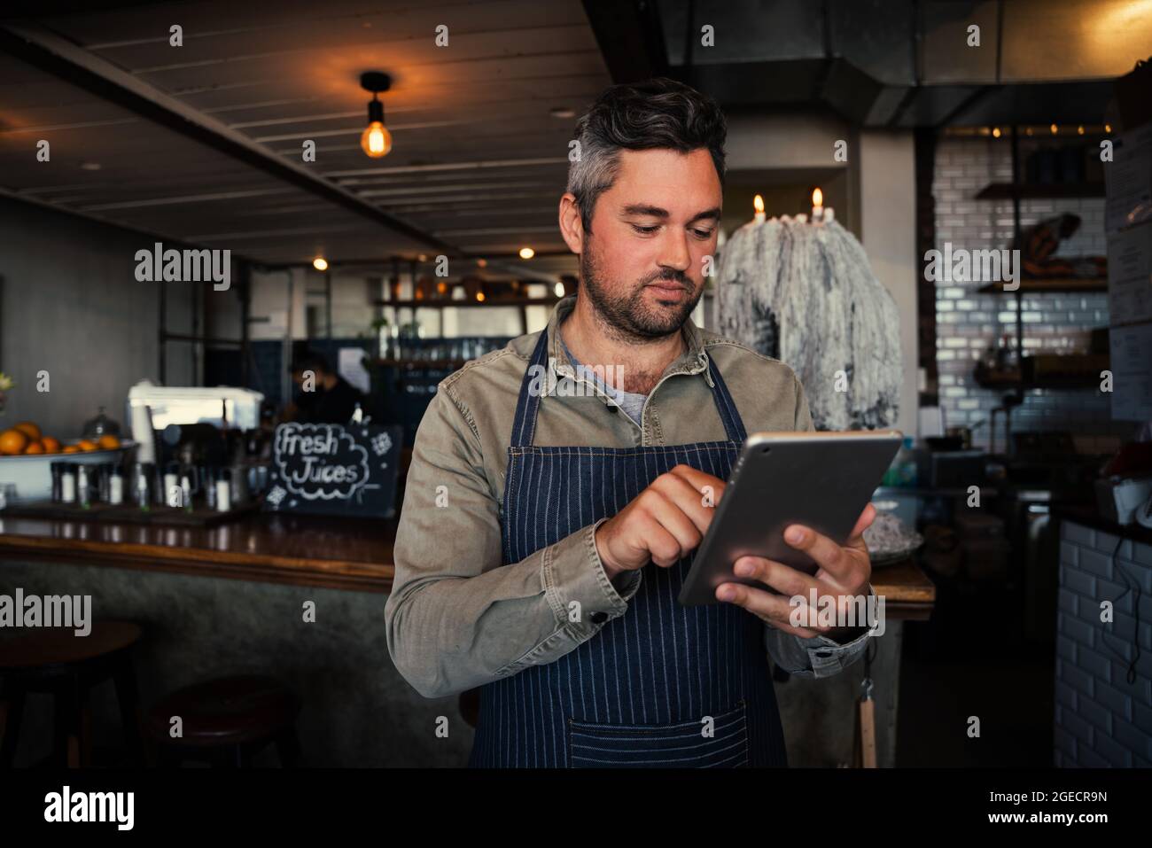 Kaukasischer Kellner scrollt durch das Online-Menü und steht in einem trendigen Café, wo er Bestellungen vorbereitet. Stockfoto