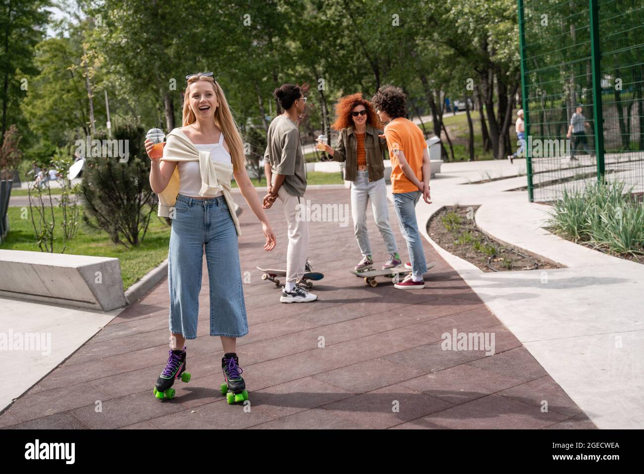 Happy Roller Skater steht mit Cocktail in der Nähe von multiethnischen Freunden Stockfoto