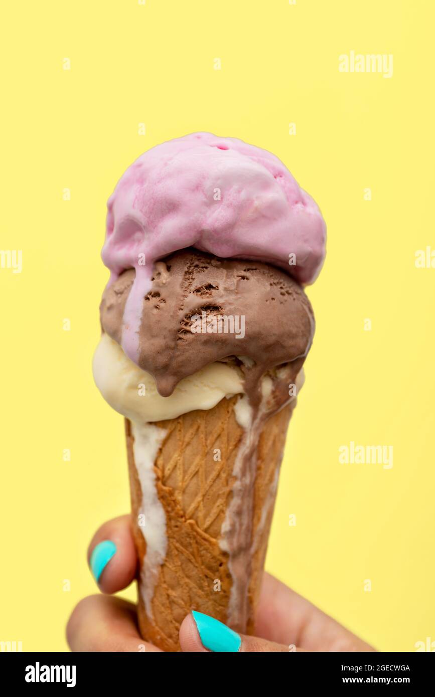 Die Hand einer Frau hält einen Eiskegel, der auf einem gelben Hintergrund schmilzt Stockfoto