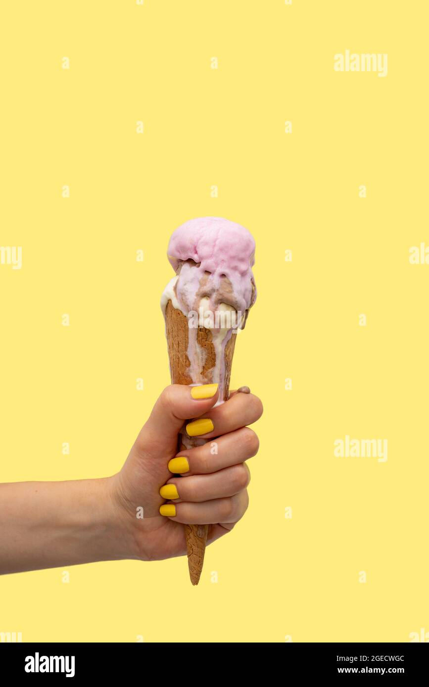 Die Hand einer Frau hält einen Eiskegel, der auf einem gelben Hintergrund schmilzt Stockfoto