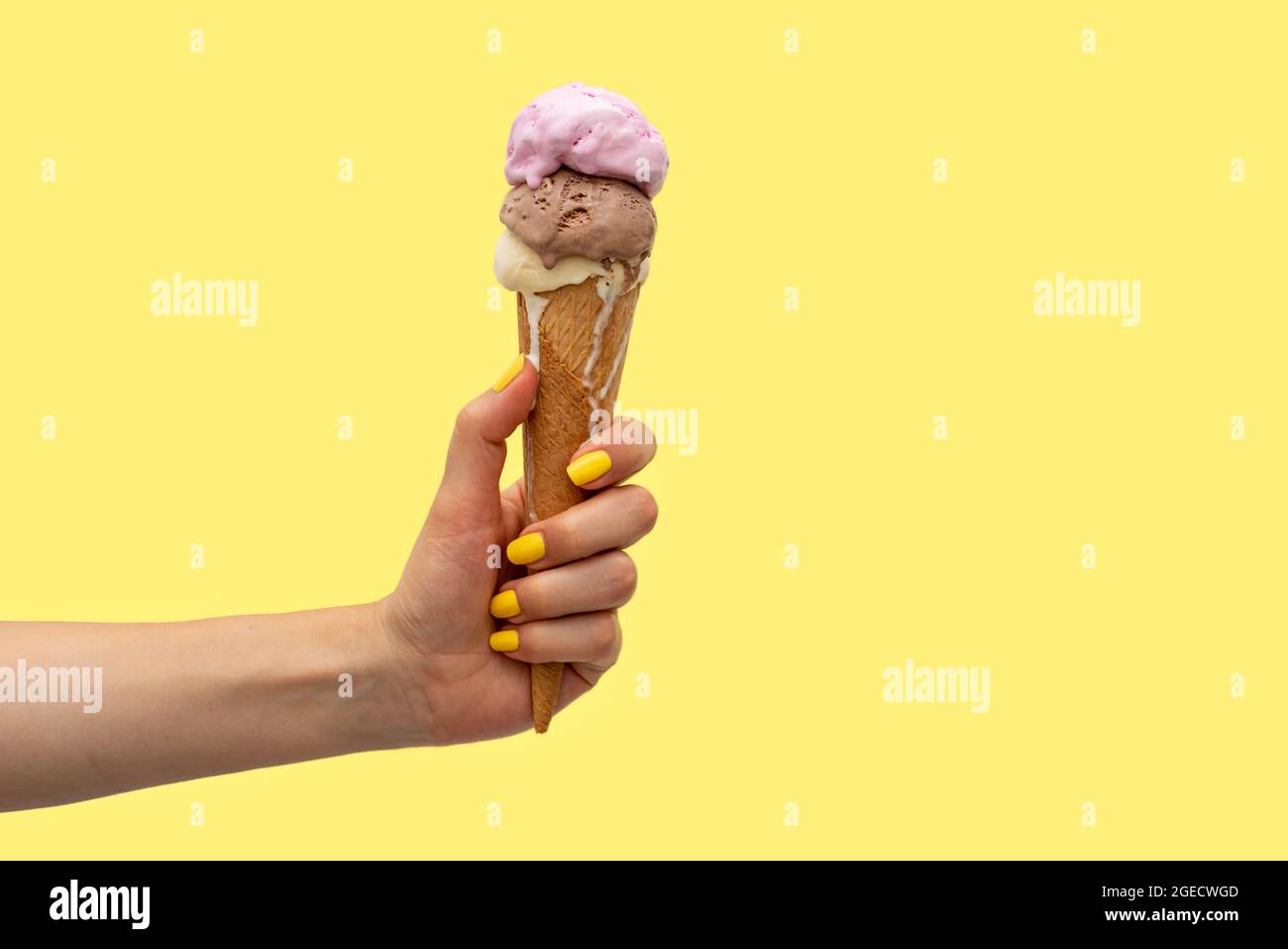 Die Hand einer Frau hält einen Eiskegel, der auf einem gelben Hintergrund schmilzt Stockfoto