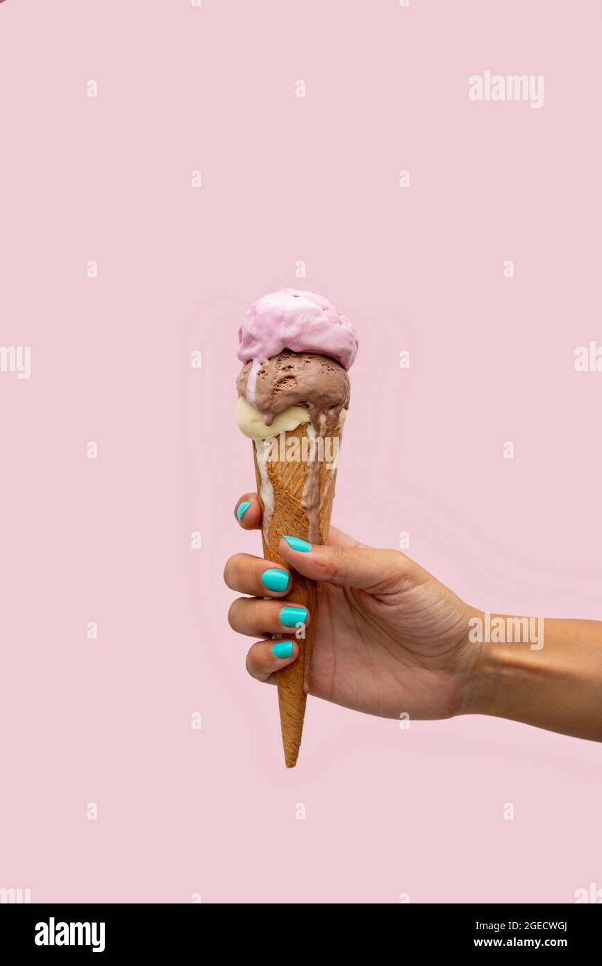 Die Hand einer Frau hält einen Eiskegel, der auf einem rosa Hintergrund schmilzt Stockfoto
